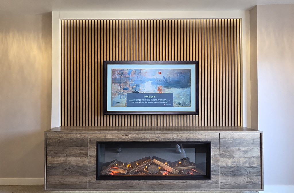 Fire integrated into a wood-effect cabinet beneath a slatted TV wall
