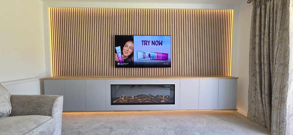 Electric fire built into a long grey cabinet beneath a timber top and illuminated slatwall